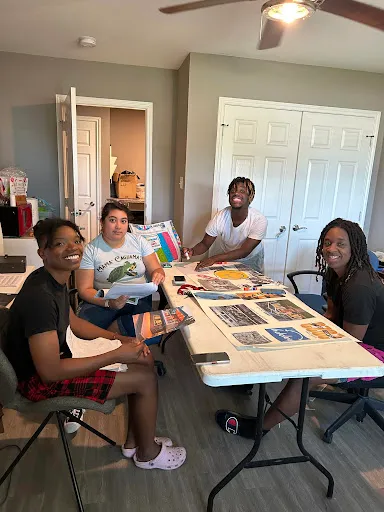 Four participants and mentors smiling around a table covered in planning materials.
